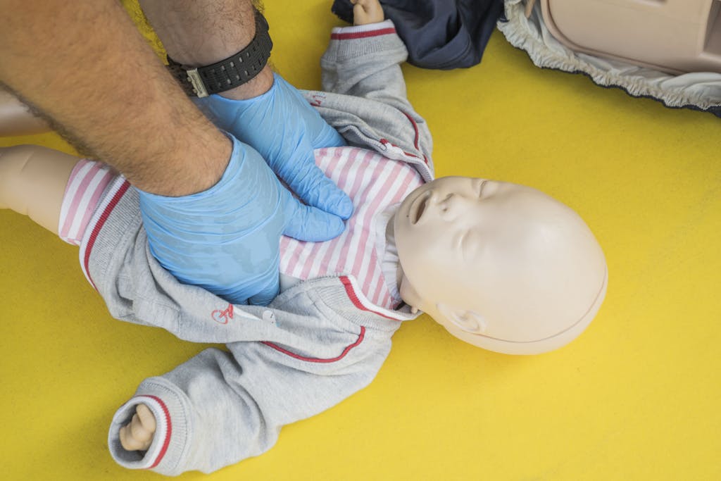 Hands performing CPR on an infant mannequin for a first aid training session.